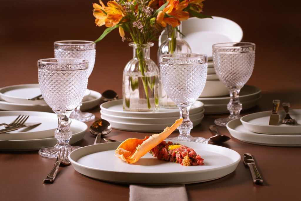 mesa posta delicada em tons de branco com copo bico de jaca transparente e flores